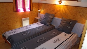 Quarto com cama, travesseiros, mesa de cabeceira, luminária na parede e janela com cortinas.