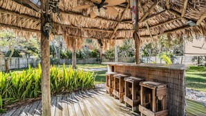 An outdoor wooden deck with a thatched roof and a bar area with stools. - 5b Resort Style Pool Home! Tiki Bar, 1 mile to Popular Beach -Tropical Paradise! (Largo)