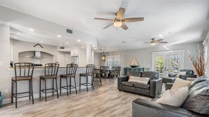 A spacious living area with a dark leather sofa, a dining table, and a kitchen area with bar stools. - 5b Resort Style Pool Home! Tiki Bar, 1 mile to Popular Beach -Tropical Paradise! (Largo)