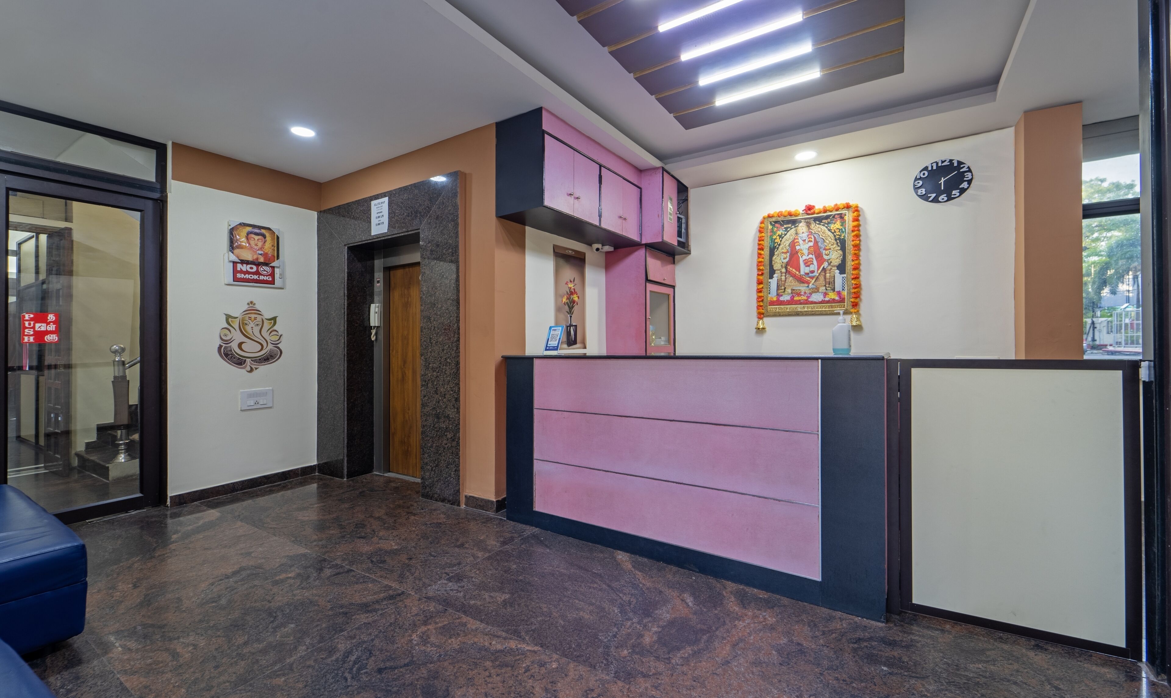 A reception area with a marble floor, a pink and black reception desk, a clock, and a religious decoration on the wall.