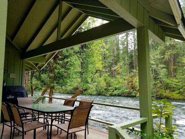 Un espace extérieur abrité, avec une table et des chaises, offrant une vue sur une rivière et une forêt.