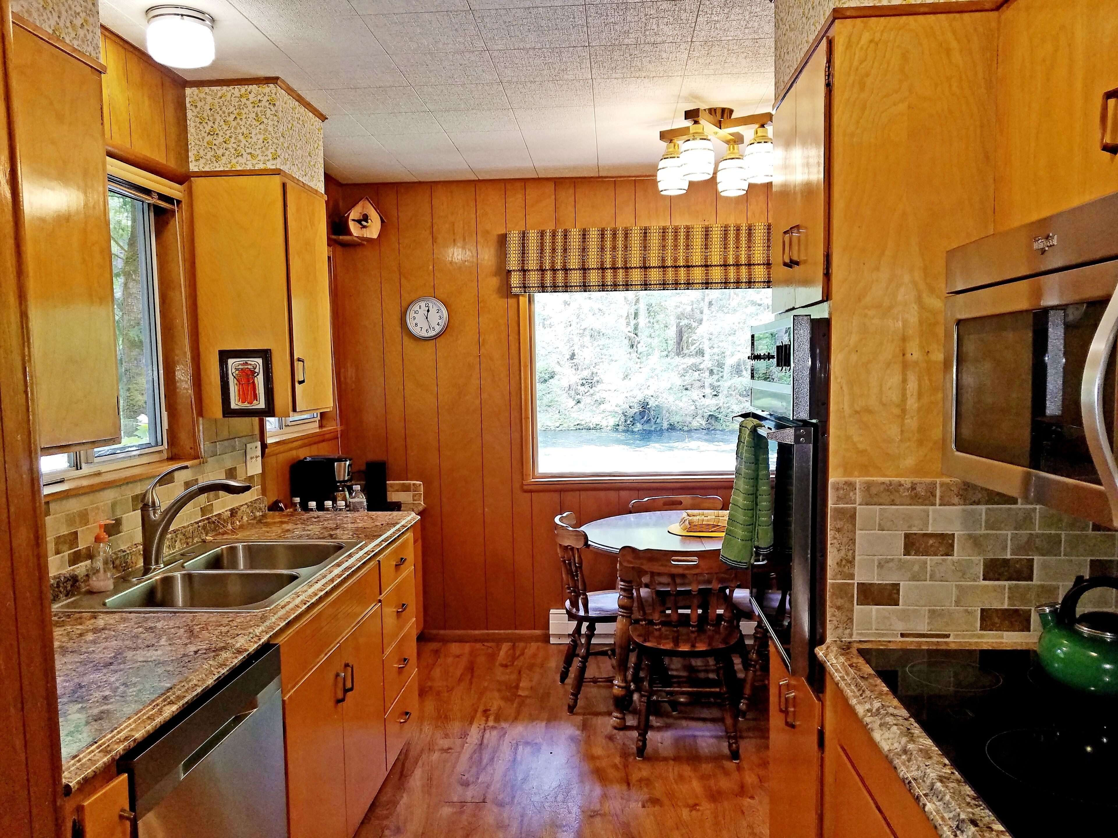 A compact kitchen with wooden cabinets, a sink, a stove, and a dining area with chairs.