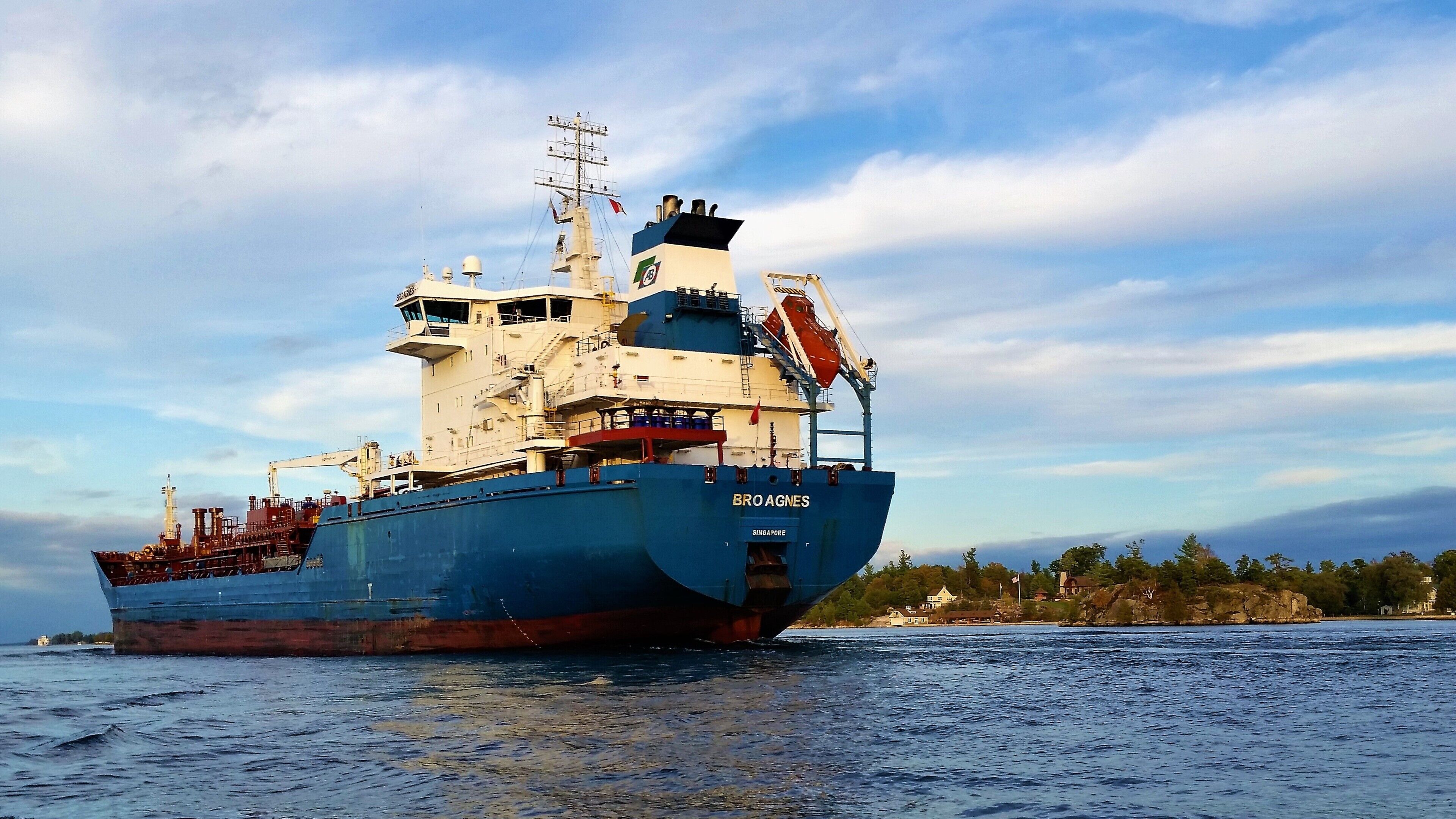 Um grande navio de carga chamado 'BRO AGNES', com uma grua e diversos equipamentos de convés, navegando em um corpo de água sob um céu claro e com uma linha costeira distante.