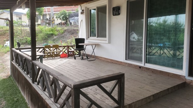 Une terrasse extérieure couverte, dotée d’une rambarde en bois, d’une table et de chaises.