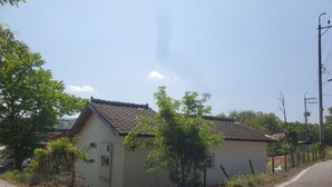Un bâtiment d’un seul étage, doté d’un toit en tuiles, entouré de verdure et bordé d’une route pavée.