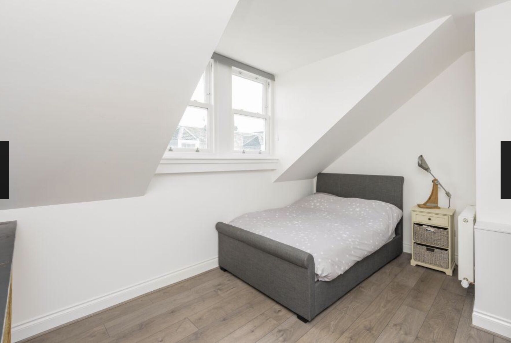 Une chambre avec un plafond en pente, un lit, une table de chevet et une fenêtre.