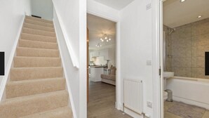 Un escalier menant à une cuisine avec un îlot central, une salle de bain avec douche et baignoire, et un couloir avec un radiateur.