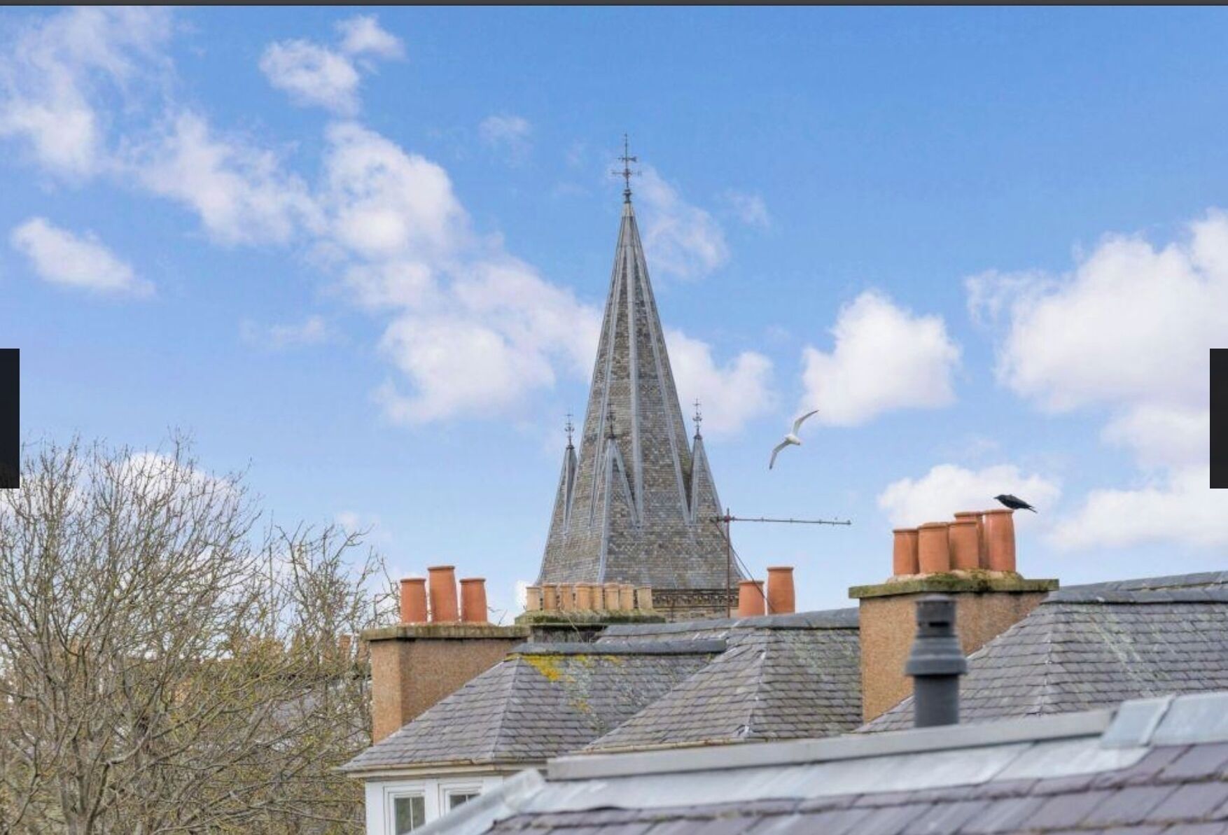 Une église dotée d’un clocher élancé et d’une girouette, entourée d’immeubles d’habitation.