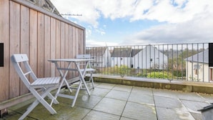 Un balcon doté d’un mur en bois, d’une rambarde en métal et offrant une vue sur des maisons au loin.