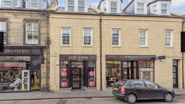 Une vue de rue avec une rangée de boutiques, dont un salon de coiffure, un studio et un magasin de vêtements.
