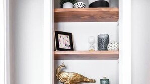 A narrow hallway with wooden shelves displaying various decorative items, including plants, sculptures, and books. - ❤️ Heart of Tech Terrace 3/2 Remodeled Near Tech (Lubbock)