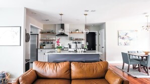A modern kitchen with a central island, a dining area with a table and chairs, and a leather sofa in the foreground. - ❤️ Heart of Tech Terrace 3/2 Remodeled Near Tech (Lubbock)