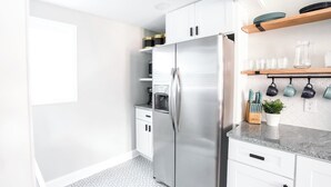 A modern kitchen with white cabinets, a stainless steel refrigerator, and a countertop with kitchen utensils and a potted plant. - ❤️ Heart of Tech Terrace 3/2 Remodeled Near Tech (Lubbock)