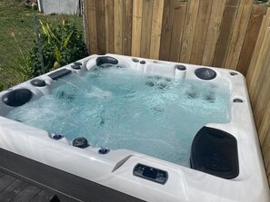 Un bain à remous doté de plusieurs jets, entouré d’une clôture en bois et de verdure.