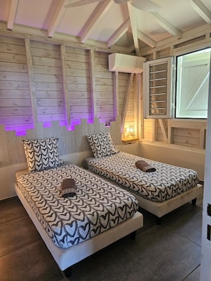 Ein Zimmer mit zwei Betten, Holzwänden, einem Fenster mit Jalousien und einem Deckenventilator.
