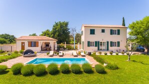 Ein zweigeschossiges Haus mit Swimmingpool, einer Terrasse mit Liegestühlen und einem Garten.