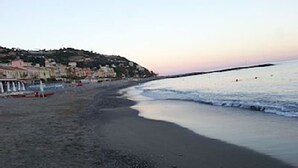 A beach with a long stretch of sand, a calm sea, and a distant shoreline with buildings. - Appartamento Vista Mare 100mq + Terrazzo 100mq + Balcone (Ospedaletti)