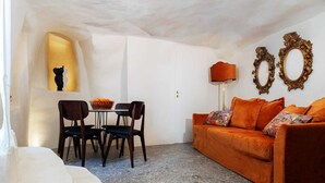Un soggiorno con divano, poltrone, un tavolo con frutta, una lampada e specchi decorativi.