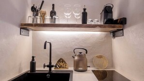 Una cucina compatta con un lavandino nero, una macchina da caffè e un bollitore sul piano di lavoro.
