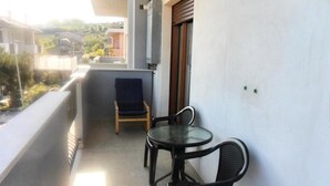 Un balcon avec une petite table et deux chaises, une fenêtre et une vue sur le quartier.