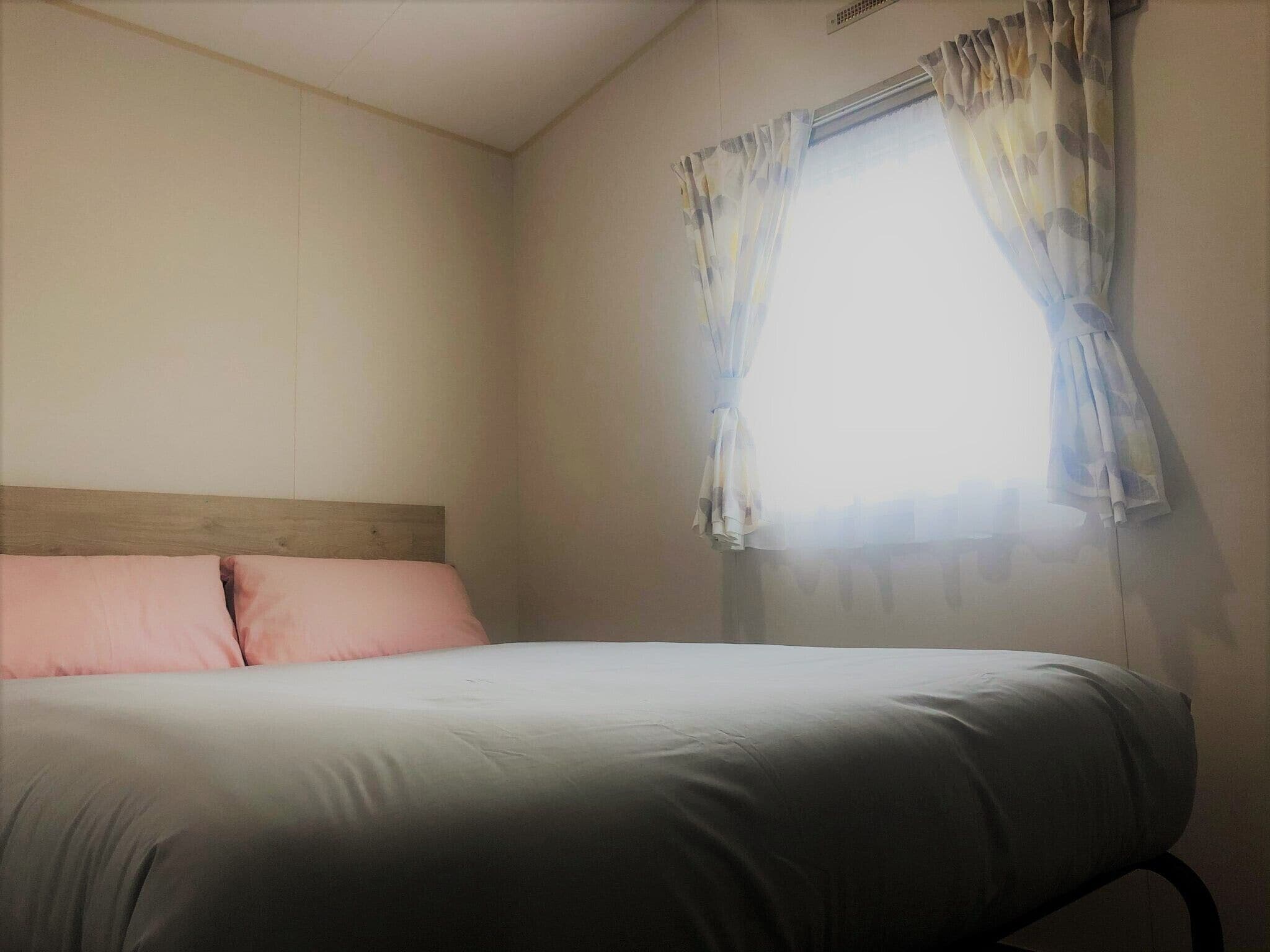 A single bed with a wooden headboard in a room with plain walls and a window with floral curtains.