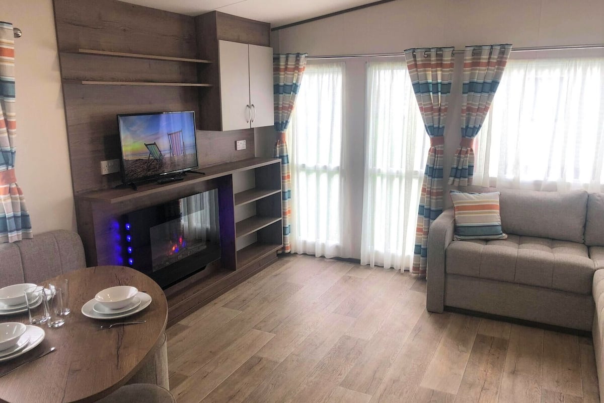 A living room with a flat-screen TV, a fireplace, a sofa, and a dining table set with plates and glasses.