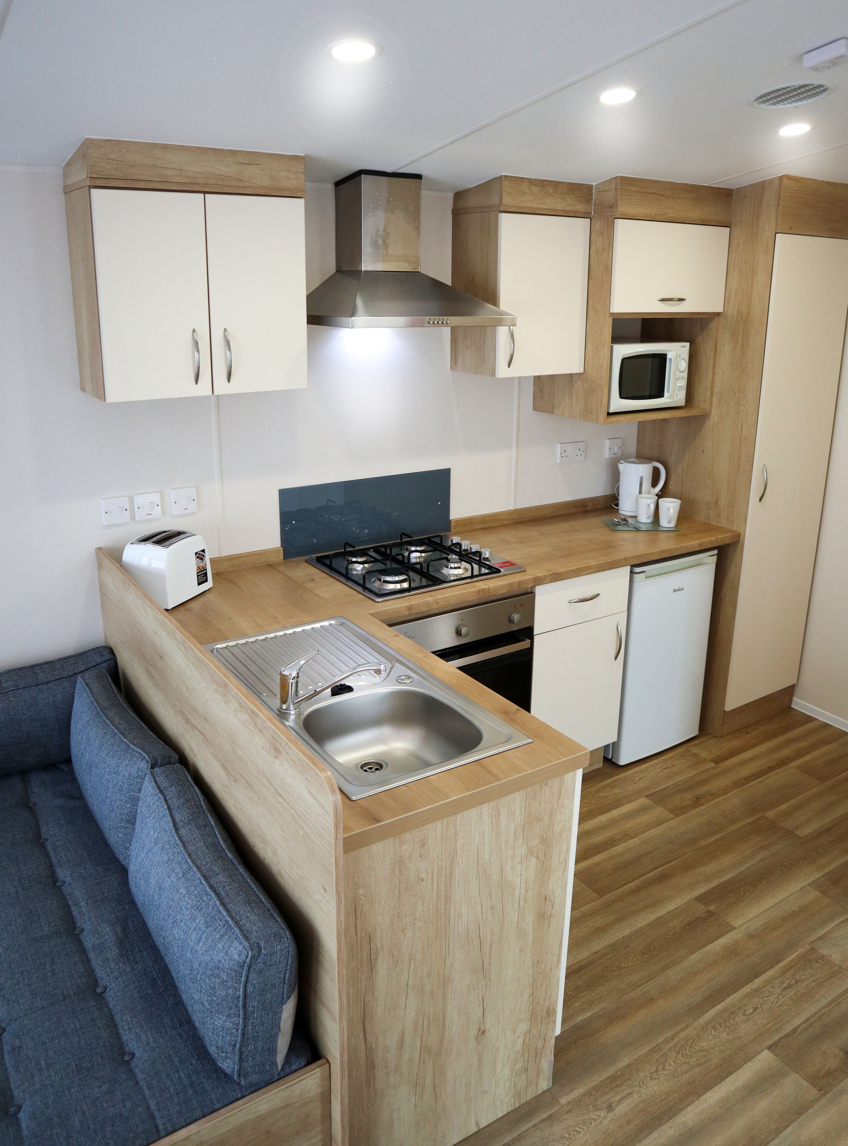 A compact kitchen with a gas stove, microwave, and a sink. There is a small seating area with a sofa and a coffee table.