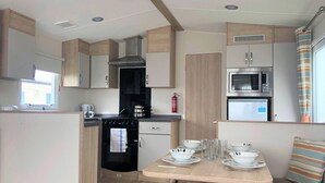 A compact kitchen with a stove, oven, microwave, and a small refrigerator. There is a dining table with chairs and a fire extinguisher mounted on the wall. - Golden Palm Resort (Skegness)