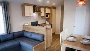 A compact living space with a sofa, a dining table with chairs, a kitchenette, and a door. - Golden Palm Resort (Skegness)