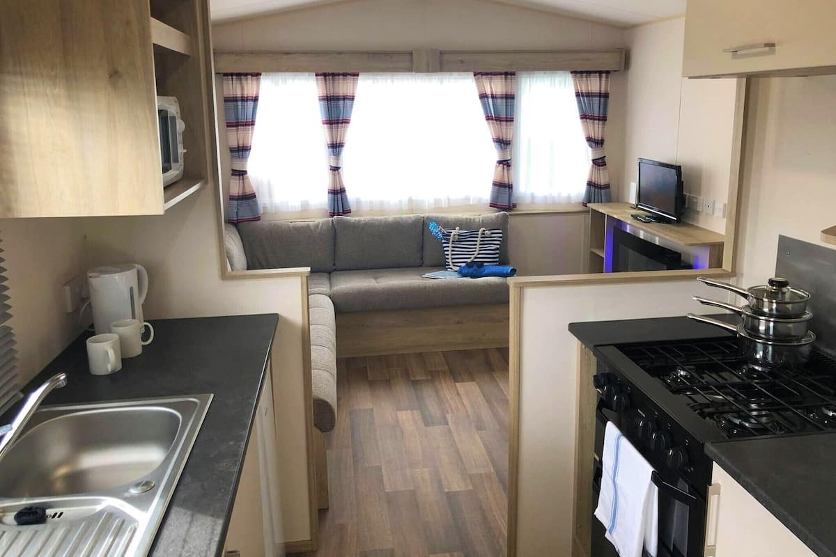A compact kitchen with a sink, stove, and microwave. A sofa is placed near the window, and a television is mounted on the wall.