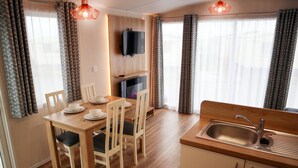 A modern kitchen with a wooden table and chairs, a built-in TV, and a sink. - Golden Palm Resort (Skegness)