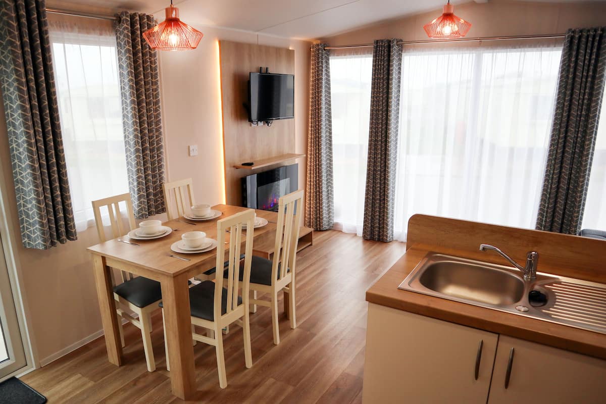 A modern kitchen with a wooden table and chairs, a built-in TV, and a sink.
