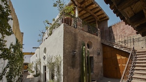 A narrow cobblestone alley with a rustic building featuring a wooden staircase, a wooden door, and potted plants. - Meson Hidalgo (San Miguel de Allende)