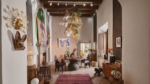 A cozy interior with a round table, chairs, a red rug, and various decorative items including a sunburst wall piece and a hanging plant. - Meson Hidalgo (San Miguel de Allende)