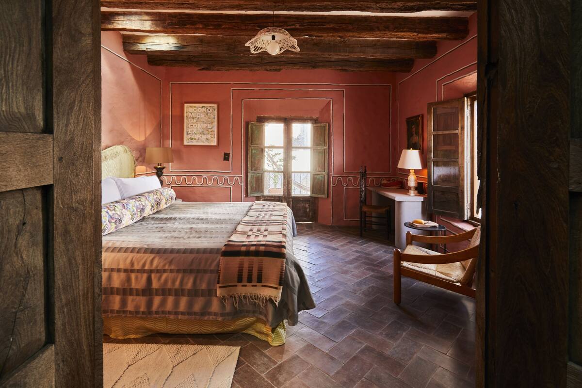A bedroom with a bed, a chair, a desk, and a window.