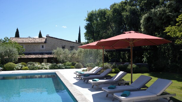 A pool with lounge chairs and a red umbrella, surrounded by greenery and a stone building. - Stone farmhouse with large pool in Ménerbes, Luberon (Ménerbes)