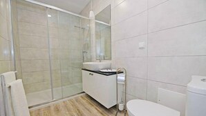 Un baño moderno con cabina de ducha de vidrio, un lavabo blanco y un inodoro.