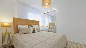 Una habitación de hotel con una cama grande, dos lámparas de noche, un espejo y suelo de madera.