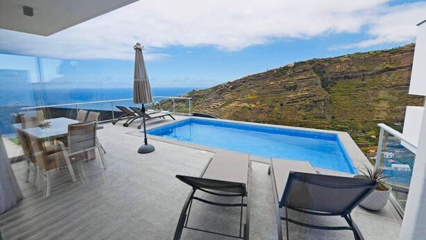Un espacio exterior moderno con piscina, mobiliario y una vista panorámica de la costa.