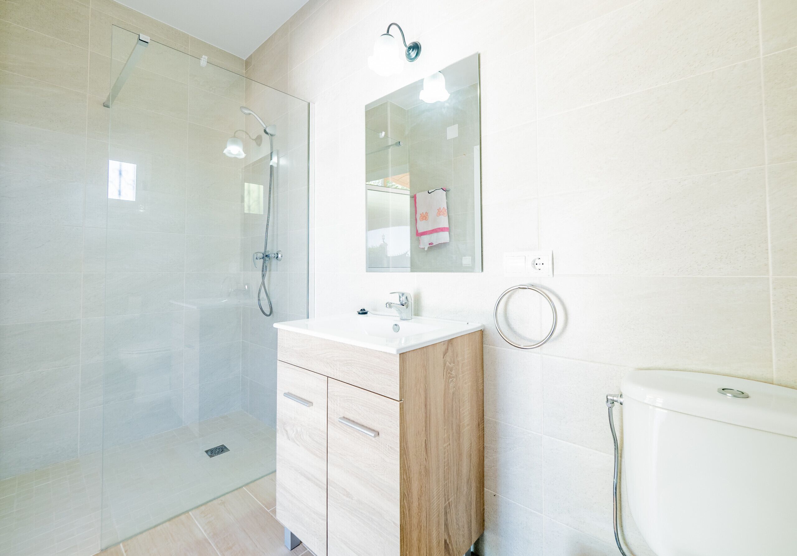 Une salle de bain moderne avec une douche à parois de verre, un meuble-lavabo en bois, un lavabo blanc et des toilettes.