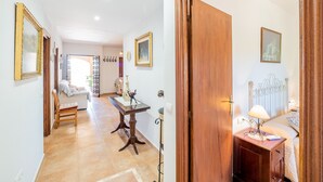 A hallway with a wooden door, a bedside table with a lamp, and a bed with a headboard.