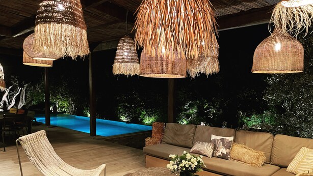 An outdoor seating area with a pool, wicker furniture, and hanging light fixtures.
