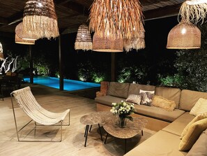An outdoor seating area with a pool, wicker furniture, and hanging light fixtures.