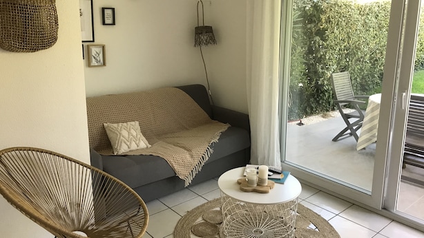 Ein Wohnzimmer mit einer Couch, einem runden Couchtisch, einem Korbstuhl und Blick auf eine Außenpatio-Terrasse.