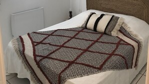 Ein Schlafzimmer mit einem Bett, einer hängenden Rattanlampe, einer Wandleuchte und einem gewebten Wandbehang.