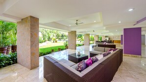 A spacious indoor area with a large wicker sofa, a glass-top coffee table, and a view of a lush garden.