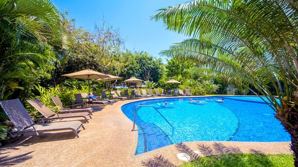A pool area with lounge chairs and umbrellas, surrounded by lush greenery.