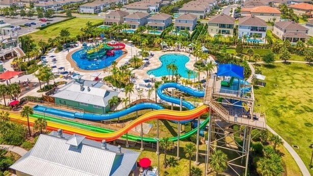 Vista aérea de un complejo turístico con varias piscinas, un parque acuático con toboganes y una zona residencial al fondo.