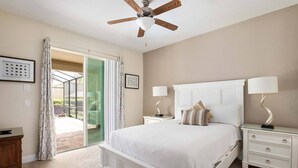 Un dormitorio con una cama, dos mesitas de noche con lámparas, un ventilador de techo y un ventanal corredero que da a un área exterior.