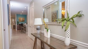 Un pasillo con una mesa de cristal, un jarrón blanco con flores amarillas y un jarrón blanco alto con diseño de celosía.
